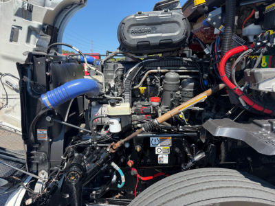 Kenworth T680 engine bay showing air intake, coolant hoses, battery, and various hoses and wiring.