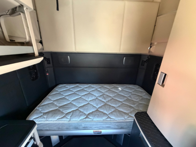 Interior sleeper cab of a Kenworth T680 showing a quilted mattress mattress, side cabinets, and bed area in neutral tones.