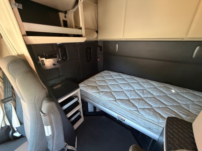 Kenworth T680 sleeper cab interior showing single bed with mattress, storage cubbies, and side panels.