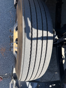 Tire and wheel assembly of a Kenworth truck showing a large radial tire and yellow wheel hub.