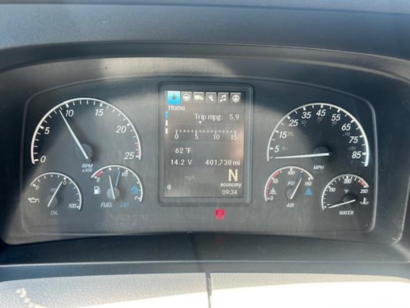 Dashboard of a Freightliner Cascadia showing instrument cluster with center digital display reading trip mpg 5.9, 62°F, 14.2 V, 401,730 mi, N economy 09:34.