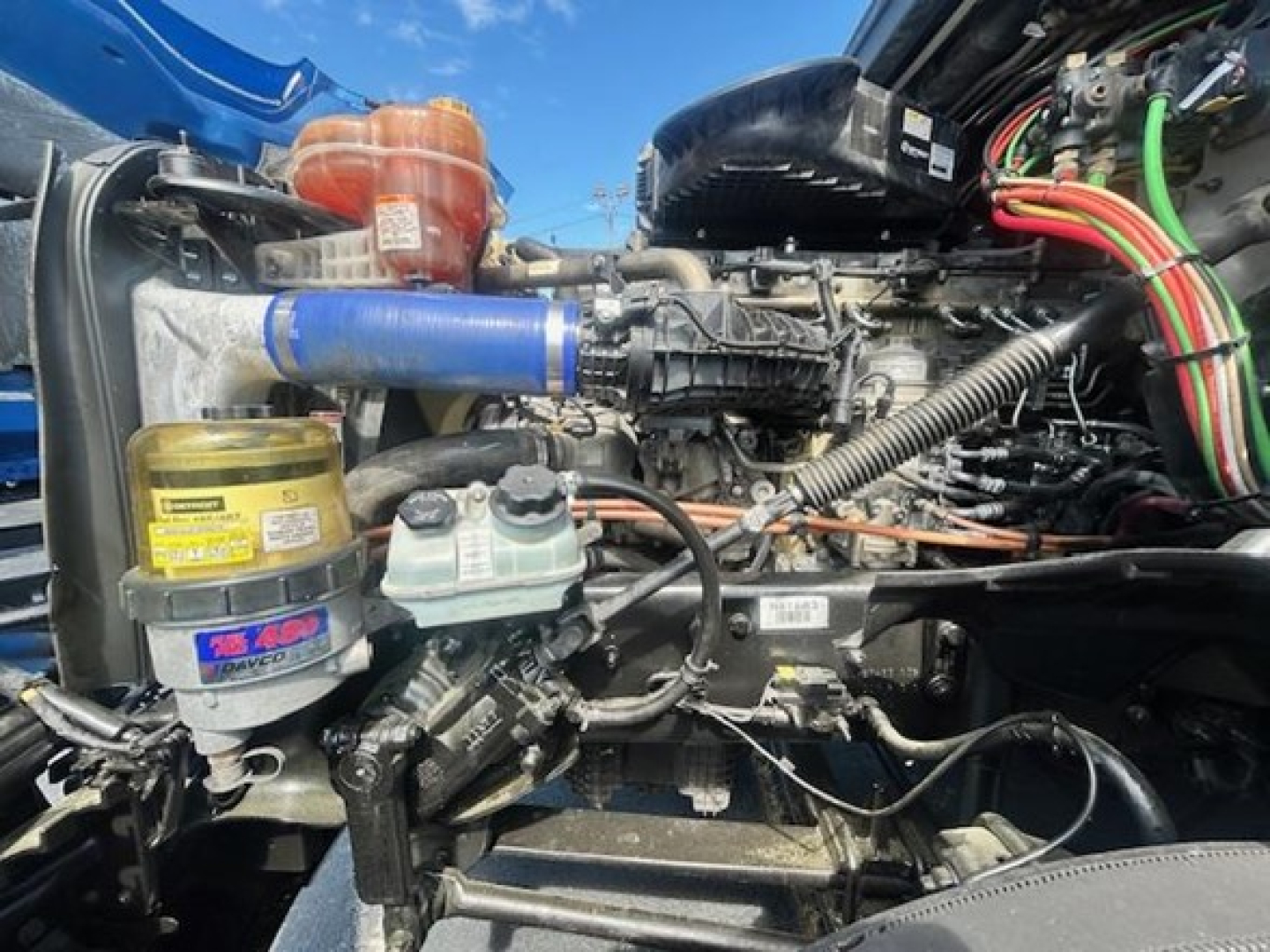 Freightliner Cascadia engine bay showing coolant reservoir, power steering reservoir, and various hoses with colorful wiring harnesses.