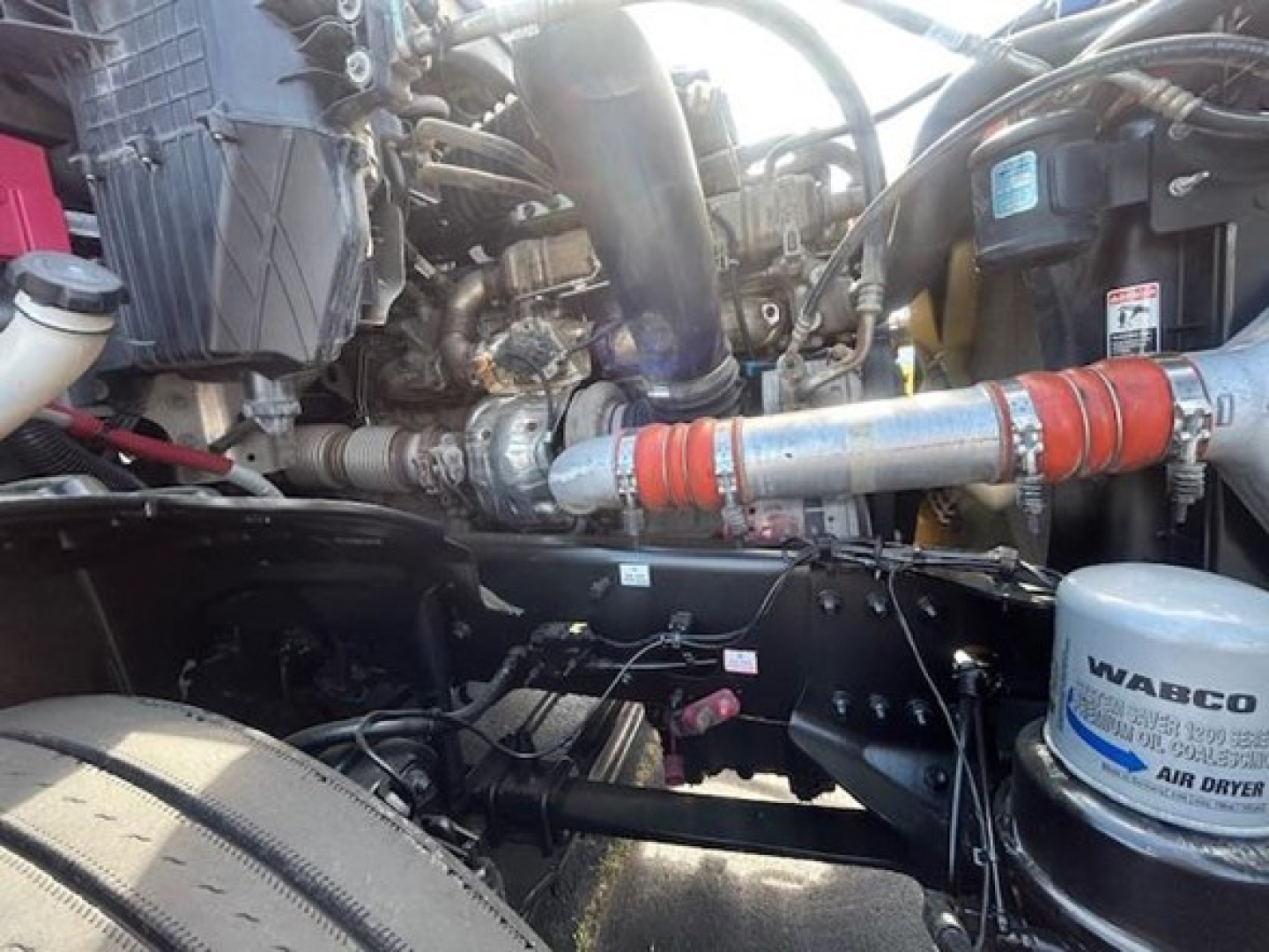 Cascadia engine bay showing air dryer canister labeled WABCO and various hoses and metal piping in the engine compartment.