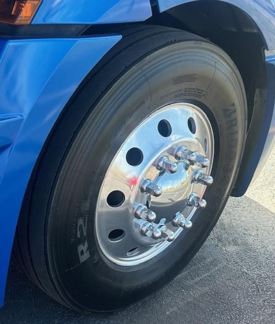 Wheel and tire close-up on a blue Freightliner Cascadia 126 front axle showing polished aluminum rim and lug nuts.
