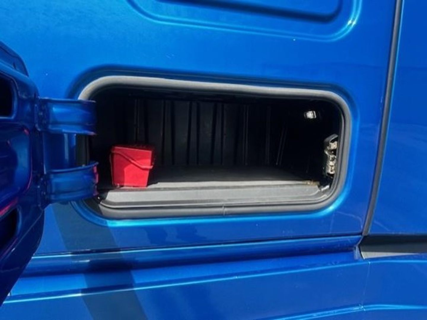Freightliner Cascadia 126 fuel door/opening showing red battery disconnect cover and storage pocket.