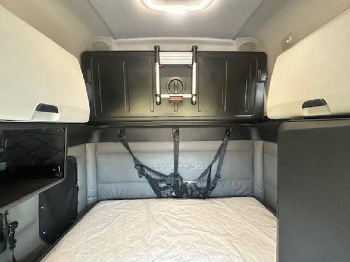 Interior sleeper cab of a Freightliner Cascadia 126 showing rear bunk area, cargo nets, and overhead storage hatch.