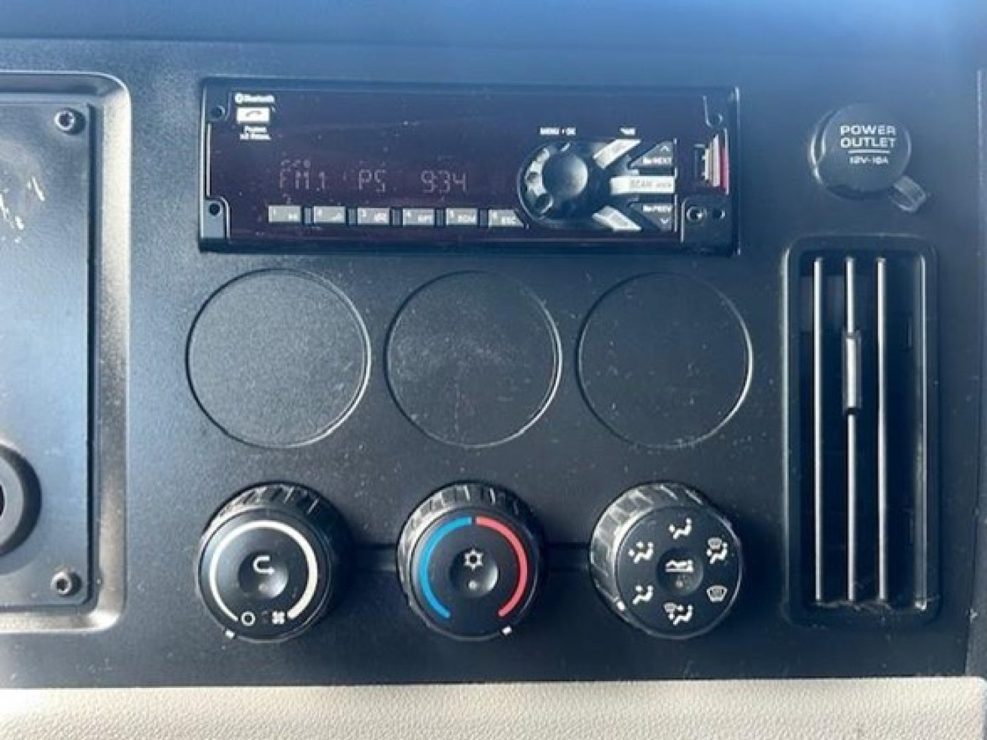 Dashboard cluster of a Freightliner Cascadia features a radio unit, three circular gauges, climate control knobs, and a power outlet. The radio display shows unreadable digits.