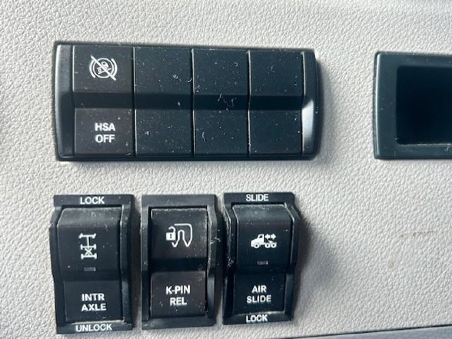 Dashboard control switches for Freightliner Cascadia showing HSA OFF and various lock/slide controls, interior switch panel.