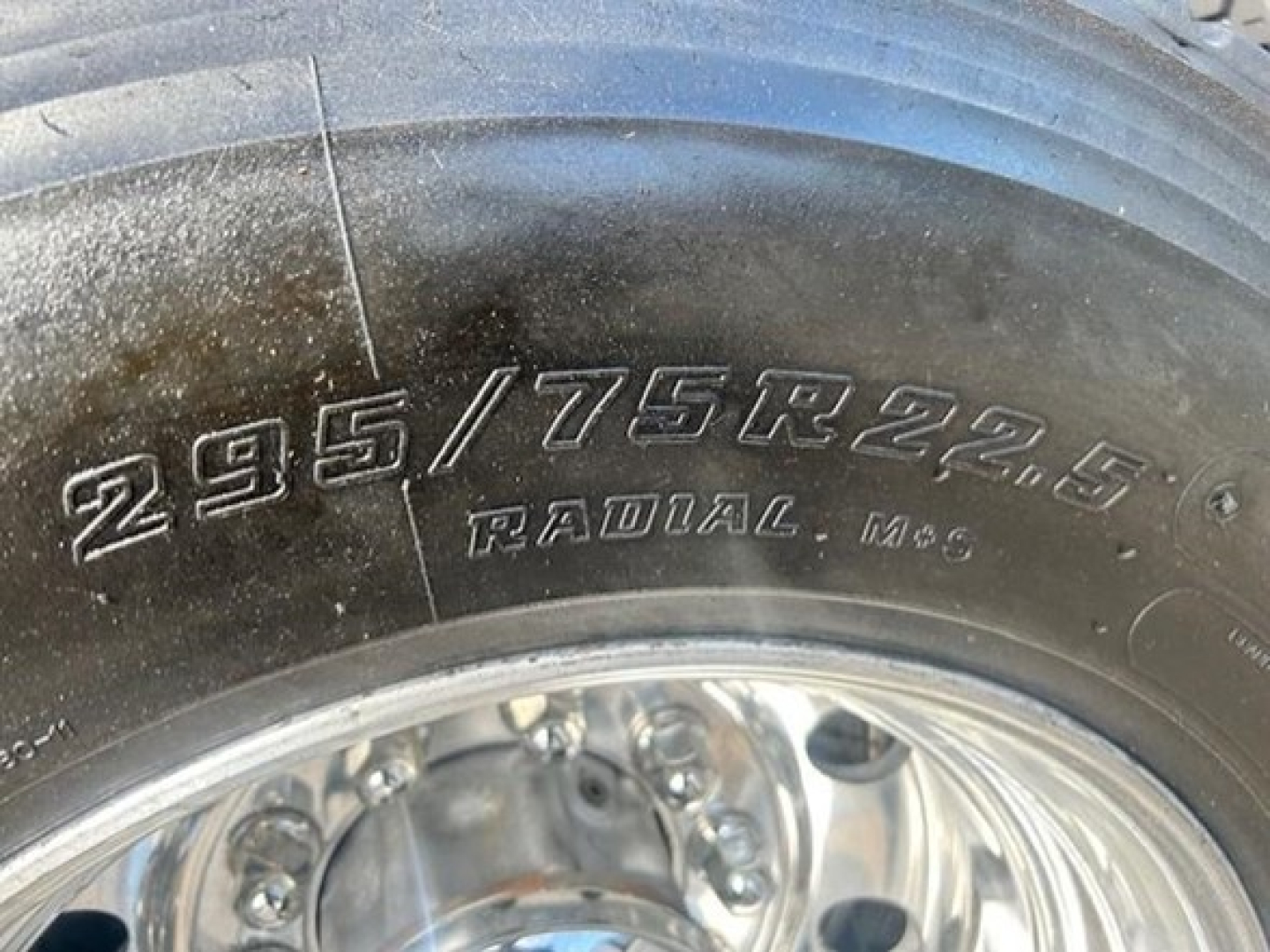Tire sidewall showing 295/75R22.5 radial MS6 on wheel; partial wheel hub and dirt visible.