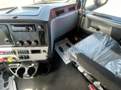Dashboard of a Freightliner Cascadia truck cab showing steering wheel, instrument panel, center stack, and front passenger seat with plastic cover.