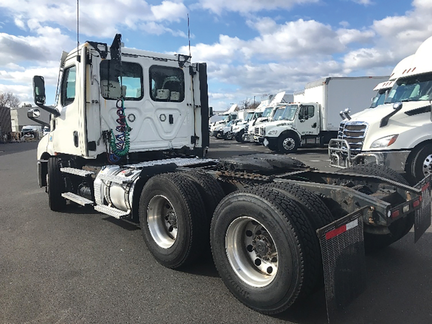 Truck chassis and cab of a Freightliner Cascadia126 tractor with dual rear axles, white cab, exposed fifth wheel area, and parked in a lot.