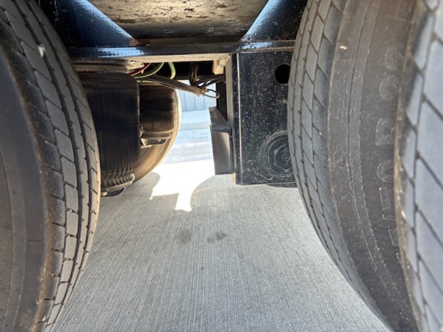 Trailer undercarriage view showing dual tires and chassis with wiring harness; close-up of frame and wheel wells.