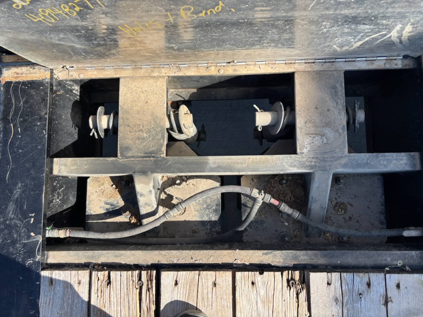 Trailer wheel hub area showing three wheel hubs and a wiring harness inside a metal frame with dirt and wear.