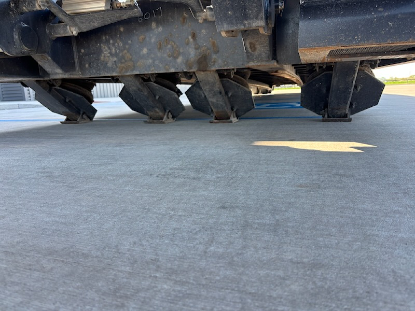 Agricultural trailer undercarriage showing metal framework and spike-type wheels; visible wear and dirt.