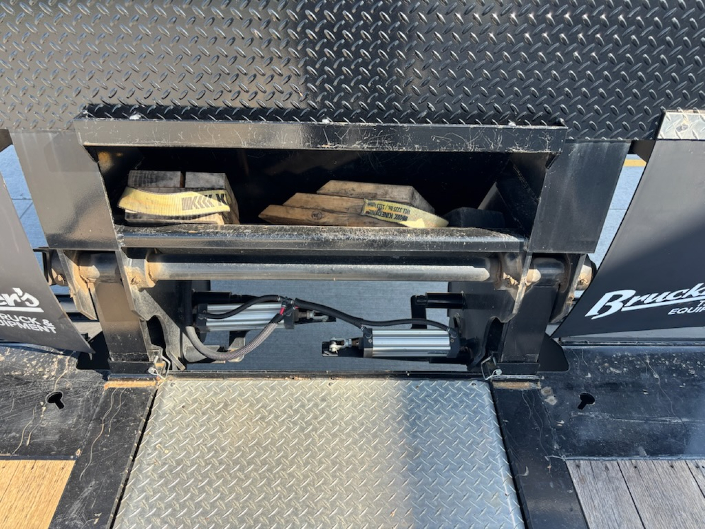Trailer undercarriage showing hydraulic components and control wiring in a diamond plate bed; label text on components partially visible.