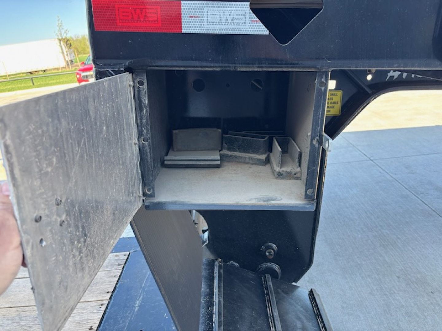 Trailer hitch area showing open storage box inside step and latch, BWS AGRN TRL branding visible on rear with red/white BWS sticker, VIN plate area nearby.