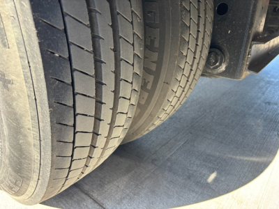 Trailer wheel group with dual tires and part of suspension visible; rubber tires show tread pattern and sidewall text.