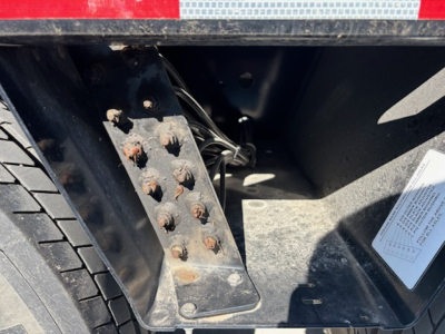 Trailer rear wheel well with black metal step and visible bolts and wiring harness inside.