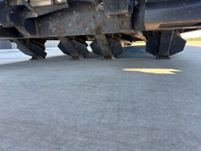Agricultural trailer undercarriage showing metal framework and spike-type wheels; visible wear and dirt.
