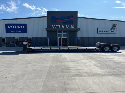 Trailer at Bruckners Parts & Sales facility with Volvo and Maek logos visible; long flatbed trailer attached to a tractor, building in background.