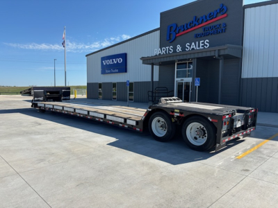 Long flatbed trailer parked outside a parts & sales building with Volvo Trucks sign.