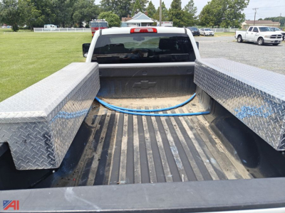 Truck bed of a Chevrolet Silverado 2500HD with diamond plate tool boxes and a blue hose in the bed, viewed from the back of a white extended cab pickup.