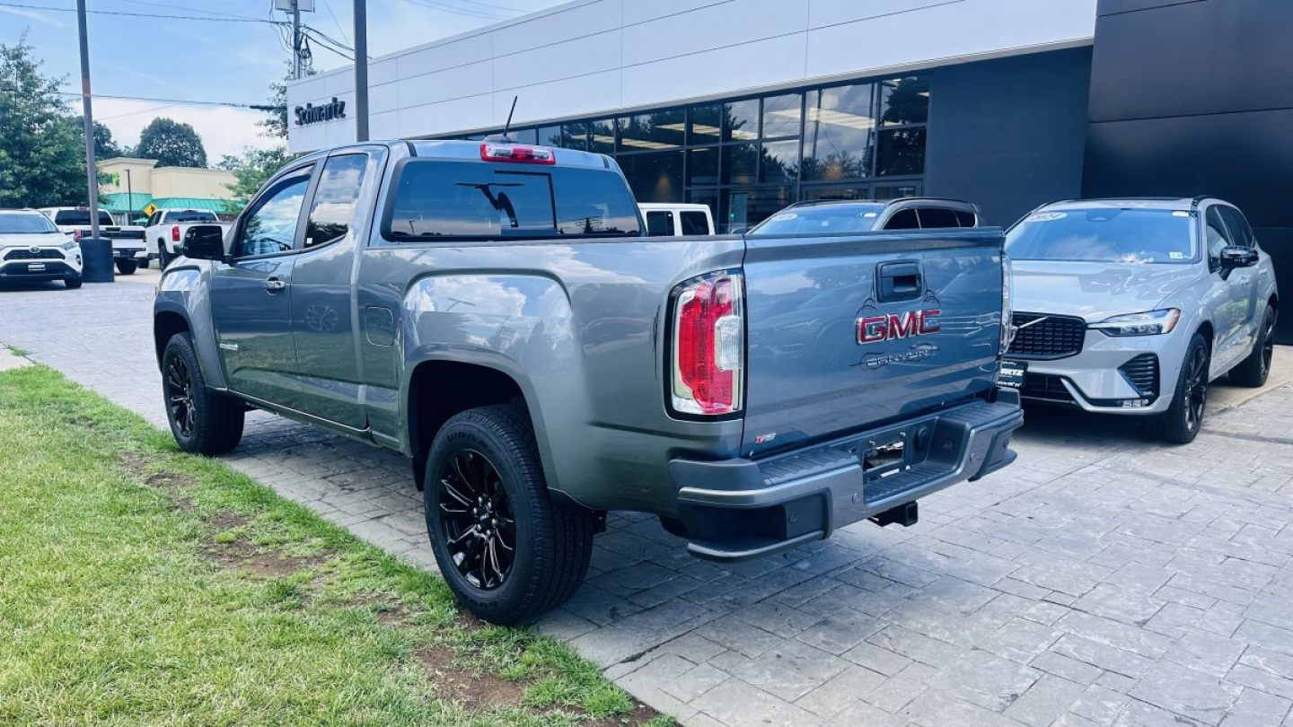 2021 GMC Canyon pickup truck in showroom lot, rear and side view with other vehicles nearby. Visible text: GMC on tailgate, Chevrolet-style taillights, dealership building in background.