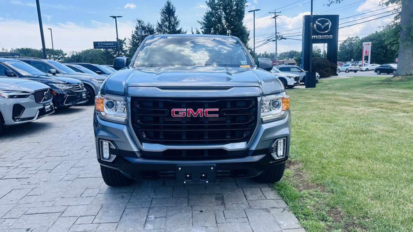 Front view of a gray 2021 GMC Canyon pickup truck parked in a dealership lot showing GMC grille with red letters and headlights.