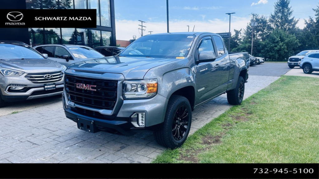 2021 GMC Canyon pickup truck parked at dealership lot; front grille with GMC badge, black wheels, chrome accents; dealership branding in top left; contact number bottom right.