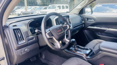GMC Canyon interior driver side view showing steering wheel with GMC badge, center console, gear shifter, and dashboard.