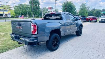 2021 GMC Canyon pickup truck rear-right view showing tailgate with GMC badge, 'CANYON' label, black wheels, light blue-gray color, dealership lot with other vehicles in background.