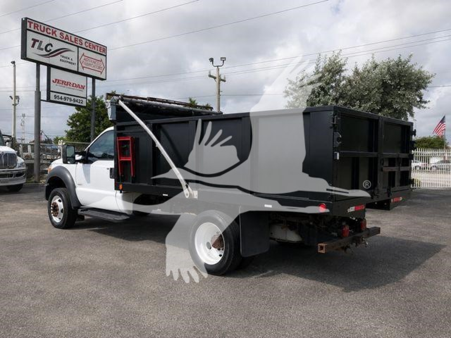 Dump truck side view showing white cab and black/gray dump bed with TLC Truck Sales Center sign in background.