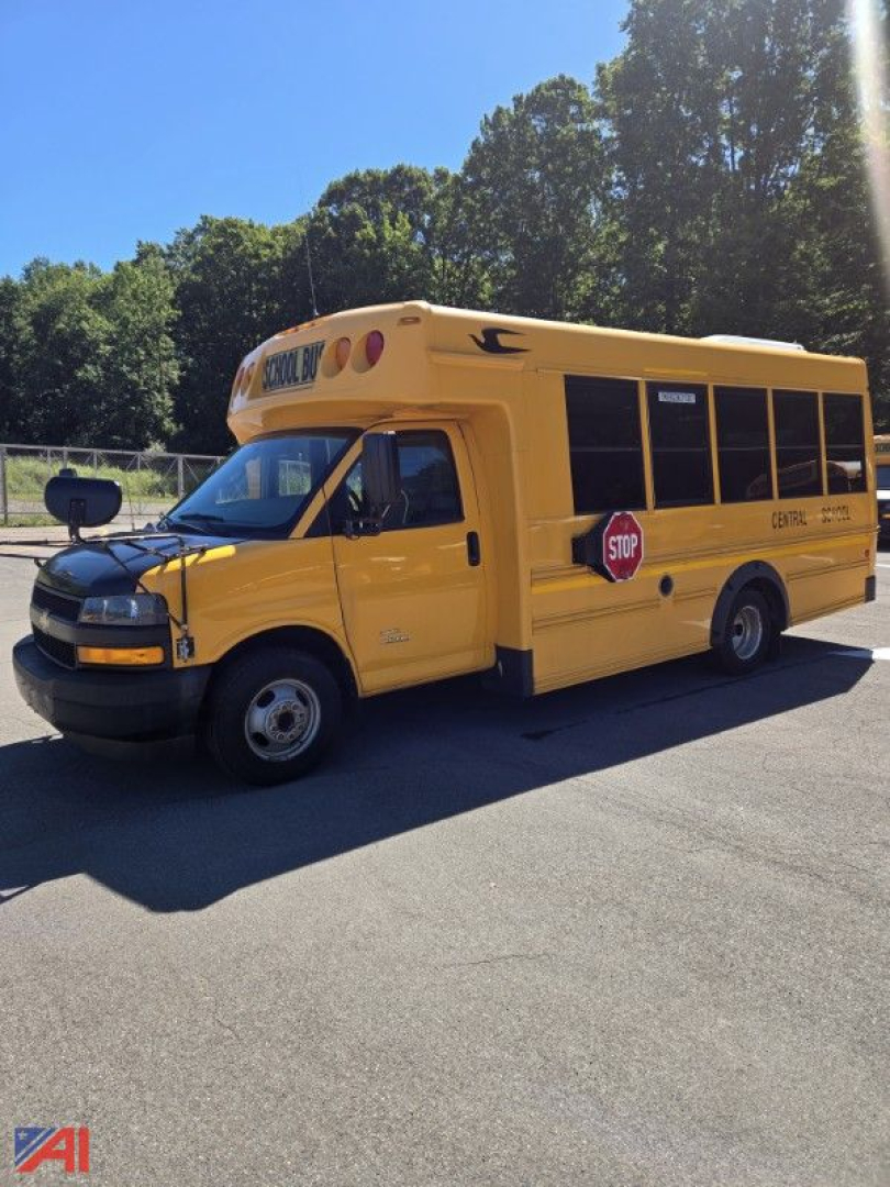 Chevrolet Express G4500 mini school bus with yellow body, stop sign, and bus lettering on side, front view parked outdoors.