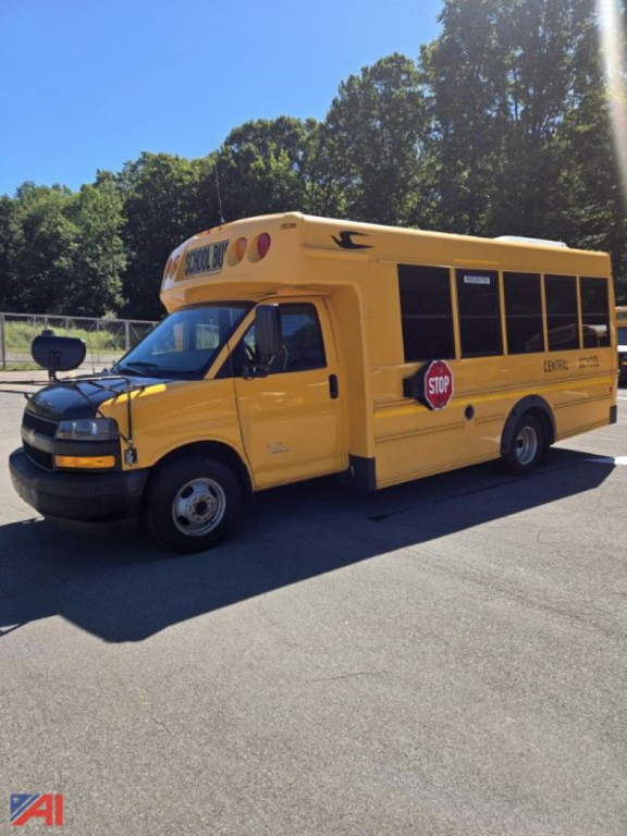 Chevrolet Express G4500 mini school bus with yellow body, stop sign, and bus lettering on side, front view parked outdoors.