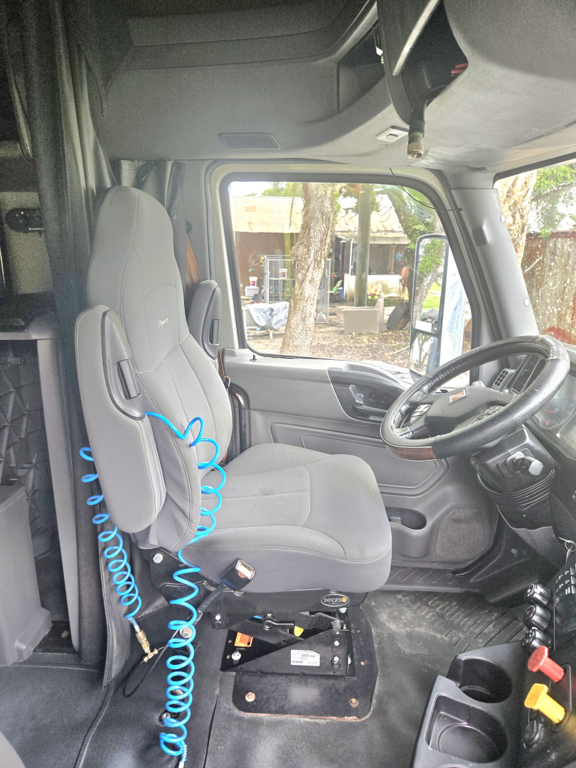 Interior cab of a used 2019 International LT625 Condo truck showing driver seat with blue coiled air hose and dashboard area