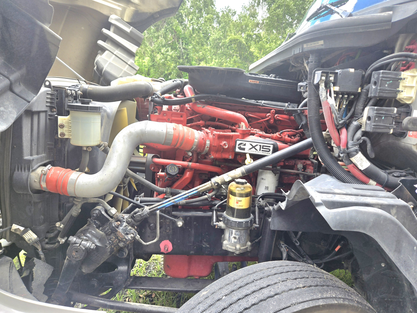 Engine bay of a 2019 International LT625 condo truck showing red engine block labeled 'X15' with surrounding hoses, wiring, and a yellow oil filter.