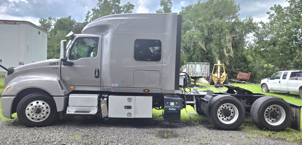 Truck chassis with sleeper cab showing International LT625 badge, side fuel tanks, and dual rear axles in a yard.