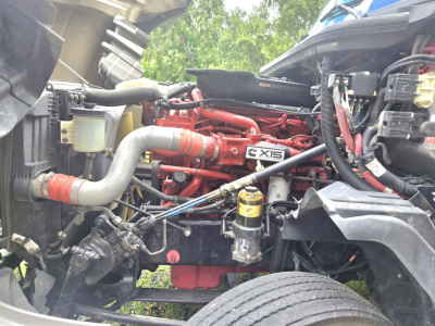 Engine bay of a 2019 International LT625 condo truck showing red engine block labeled 'X15' with surrounding hoses, wiring, and a yellow oil filter.