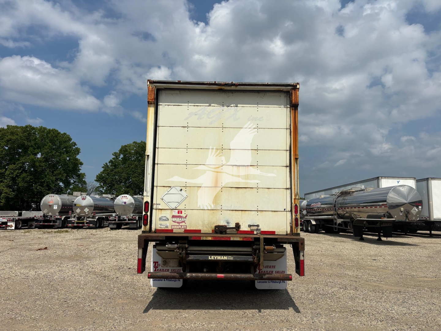 Rear view of a used Wabash trailer with a white roll-up door, stock number 7669, in an open lot with other trailers and tanker trailers nearby.