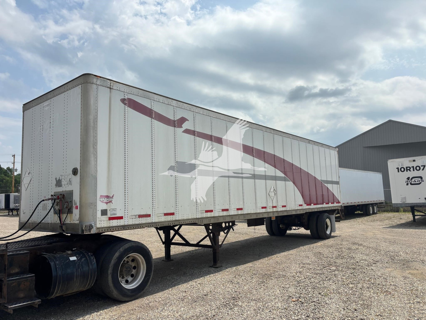 Trailer side showing large graphic artwork with maroon swoosh and bird on a white Wabash trailer, tandem axles, in a lot.