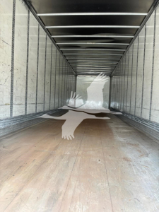 Trailer interior showing wooden floor, metal sidewalls, and overhead rails; no visible equipment labels or fluid reservoirs.