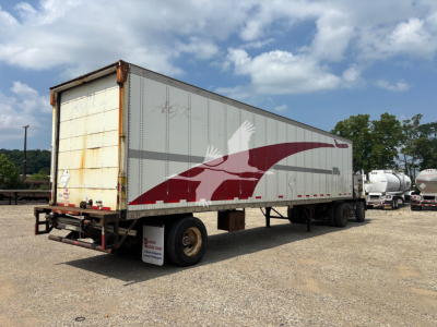 Trailer side view showing Wabash logo graphic on a white and gray trailer with rust on rear doors and a channeled undercarriage.
