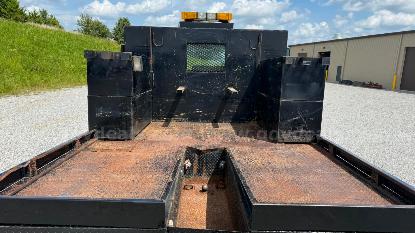 Flatbed truck bed showing rust on steel deck with rear wheel wells and a cutoff section in center; rear cab/back structure with small window grille.