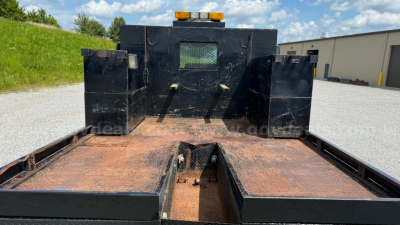 Flatbed truck bed showing rust on steel deck with rear wheel wells and a cutoff section in center; rear cab/back structure with small window grille.