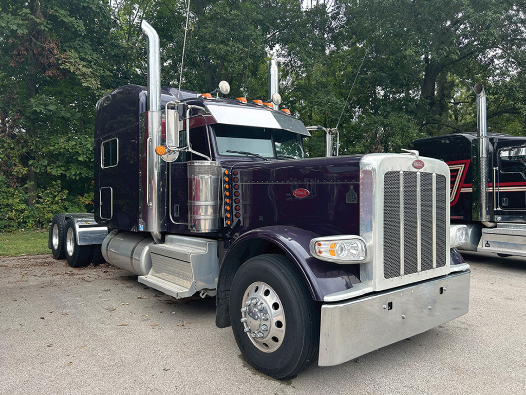 Peterbilt 389 UltraCab extended hood semi-truck in dark purple with chrome grille, large exhaust stacks, and aluminum front bumper.
