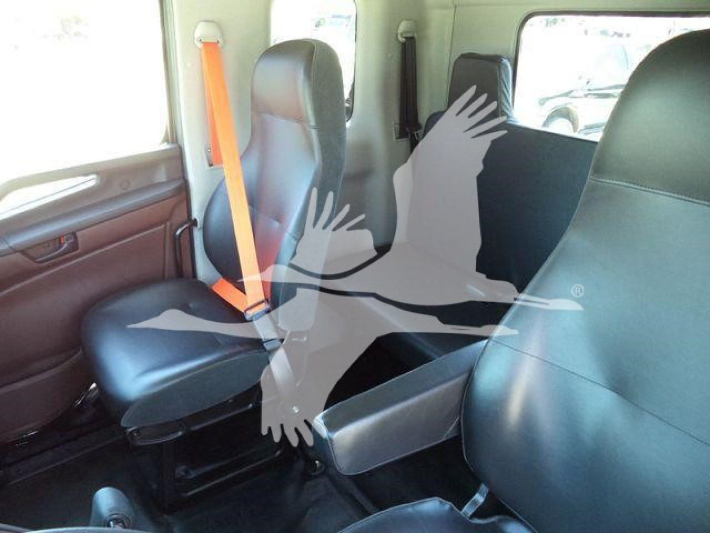 Interior of a pickup/roll-back truck cab with two front seats and a center jump seat, dark upholstery, orange seatbelt bib, windows on sides.
