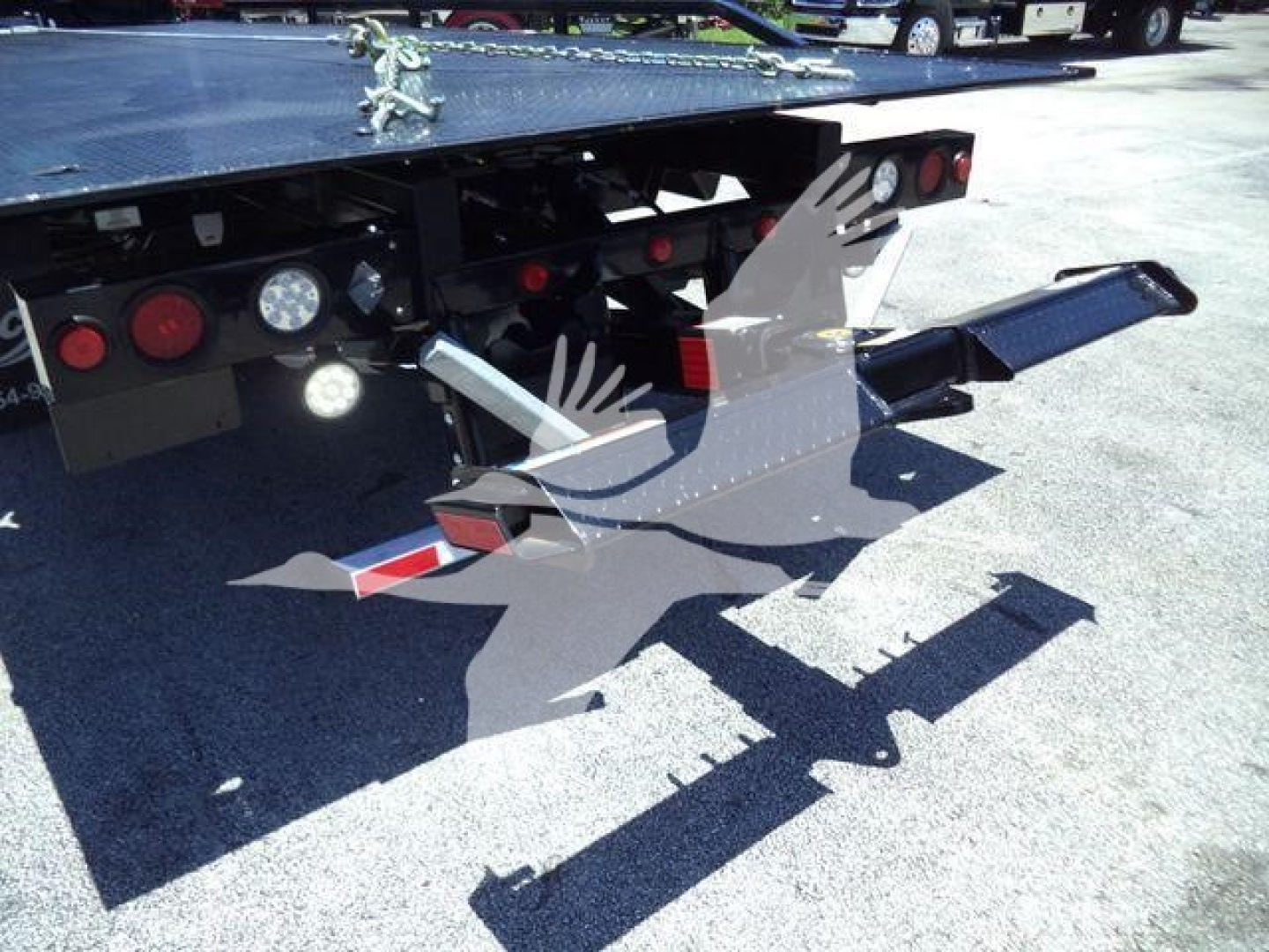 Back of a rollback tow truck showing mounted wheel-lift arms and hydraulic components with reflectors and taillights.