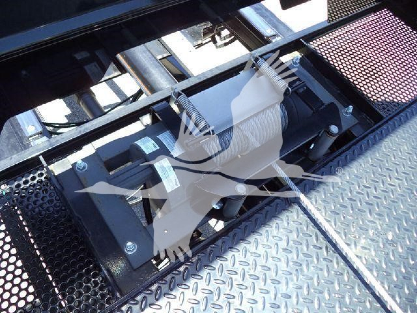Tractor unit winch/recovery equipment in a truck bed showing winch drum and motor mount with metal diamond plate surface.