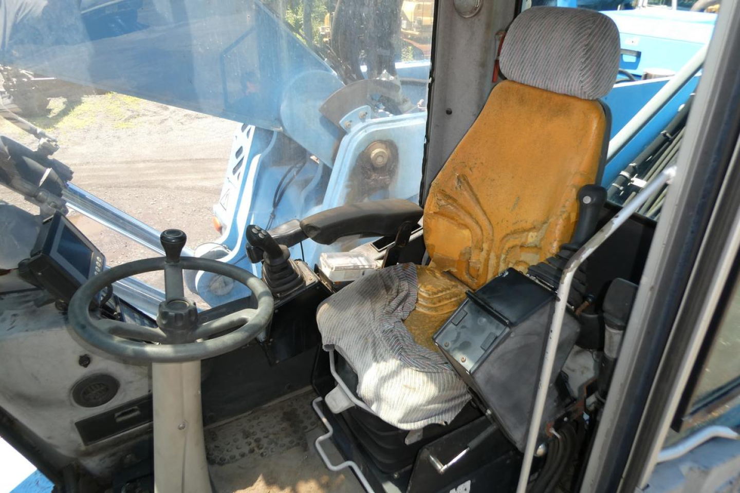 Excavator or loader cabin interior with yellow seat and steering wheel, control levers, and windshield; worn upholstery and operator seat in view.