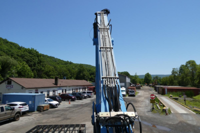 Overview of a Terex MHL350D at a yard, raised boom with hydraulic lines visible; surrounding buildings, parked vehicles, and a stop sign in the distance.